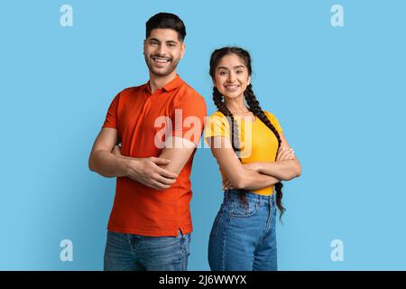 Coppia allegra Millennial Medio Oriente in piedi con le braccia piegate su sfondo blu Foto Stock