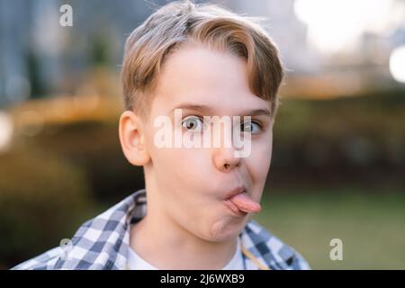 Un teenager malizioso fa i volti alla fotocamera, si stacca la lingua e si indulge. Foto Stock