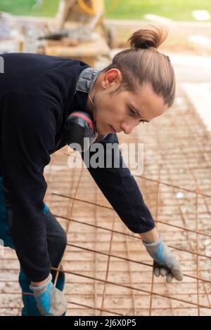 Giovane apprendista dell'uomo del hipter che lavora nella costruzione che mette la griglia di rete di ferro arrugginita sul pavimento Foto Stock