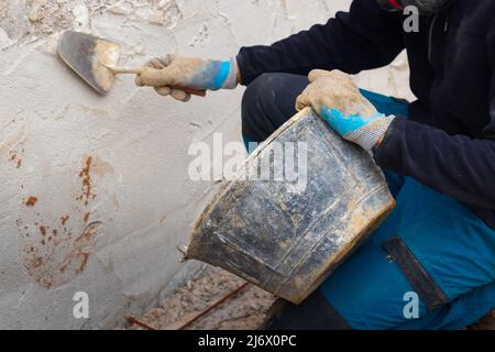 Uomo irriconoscibile che applica calcestruzzo sulla facciata della casa Foto Stock