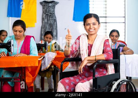 Donna sorridente felice con disabilità che mostra i pollici in su il gesto ai vestiti usando la sedia a rotelle - concetto del proprietario di piccola impresa, ispirazione e. Foto Stock