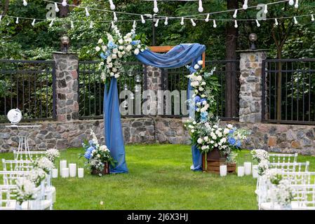 Un luogo per una cerimonia nuziale all'aperto, con un'area salotto per gli ospiti, decorata con sedie. Rustico arco in legno decorato con tessuto blu, fiore Foto Stock