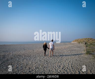 Una coppia fotografata da dietro camminando a mano lungo una spiaggia di sabbia deserta in una giornata luminosa di sole. Foto Stock