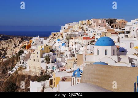 Oia, Santorini, Isole Greche, Grecia - Chiese con cupole blu, case, negozi e altri edifici bianchi sulla scogliera in un sole abbagliante e luminoso Foto Stock