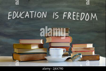 istruzione, apprendimento, conoscenza, business, concetto con mucchio di libri, tazza di caffè e slogan educazione è libertà, spazio di copia gratuito Foto Stock