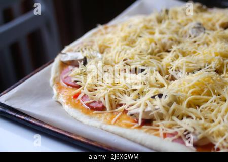 Defocalizzare in primo piano la pizza intera con mozzarella grattugiata. Defocalizzare gli ingredienti sfocati per la pizza sull'impasto. Spazio di copia. Cucina italiana b Foto Stock
