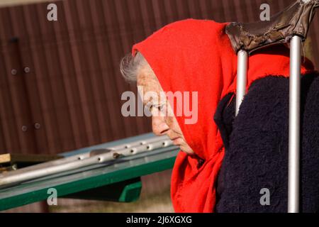 Defocus donna Ucraina anziana in scialle rosse con stampelle seduti all'esterno. Donna di 85 anni. Persona sola. Primo piano. Sfocato. Gente triste. Demen Foto Stock