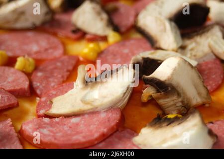 Defocalizzare gli ingredienti del primo piano per la pizza sull'impasto. Salsa di pomodoro rosso, salsicce, mais dolce. Pizza italiana fatta in casa. Home culinario. Sfocato. Cucina italiana Foto Stock