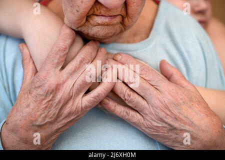 la nonna matura femmina tiene le mani del nipote, che la abbraccia da dietro. Il concetto di amore e cura. Movimento lento Foto Stock