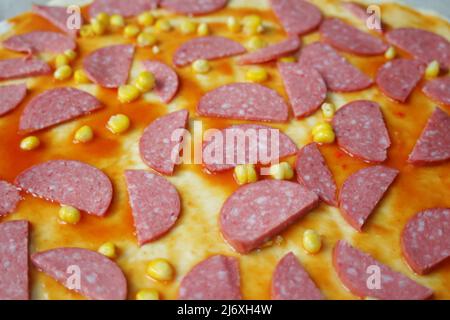 Defocalizzare gli ingredienti del primo piano per la pizza sull'impasto. Salsa di pomodoro rosso, salsicce, mais dolce. Pizza italiana fatta in casa. Base di Margarita. Home culinario. Superiore Foto Stock