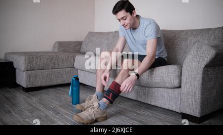 Il ragazzo mette un bendaggio a compressione sul ginocchio ferito. Preparandosi per le attività sportive, il punto dolente è evidenziato in rosso Foto Stock