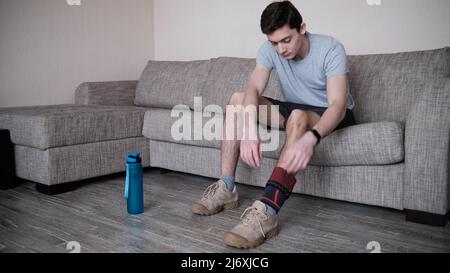 Il ragazzo mette un bendaggio a compressione sul ginocchio ferito. Preparandosi per le attività sportive, il punto dolente è evidenziato in rosso Foto Stock