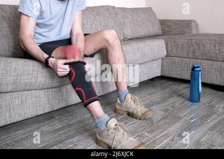 Il ragazzo mette un bendaggio a compressione sul ginocchio ferito. Preparandosi per le attività sportive, il punto dolente è evidenziato in rosso Foto Stock