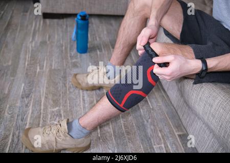 Il ragazzo mette un bendaggio a compressione sul ginocchio ferito. Preparandosi per le attività sportive, il punto dolente è evidenziato in rosso Foto Stock