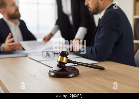 Il gavel del giudice su un tavolo di legno e la gente che lavora con i documenti nello sfondo Foto Stock