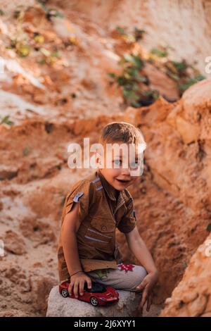 Un ragazzino sedette su una roccia tra la sabbia. Foto Stock