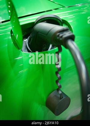 Primo piano di un ugello di ricarica rapida di tipo 2 inserito nella presa di carica di un veicolo elettrico di conversione EV Porsche verde Foto Stock