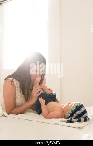 La giovane madre latina bacia i piedi del bambino e li annidano sul letto di casa Foto Stock