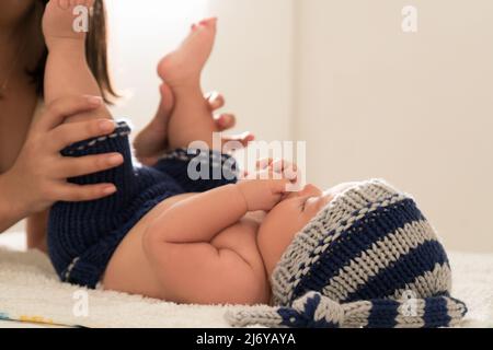 La giovane madre latina bacia i piedi del bambino e li annidano sul letto di casa Foto Stock