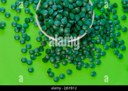 Spirulina pills in a round ciotola.Green spirulina compresse su sfondo verde. Vitamine e supplementi dietetici Foto Stock