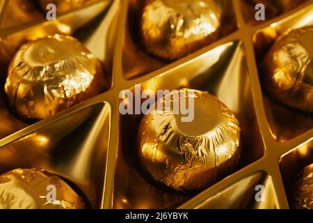 Primo piano di bononi di cioccolato avvolti in lamina d'oro nella loro scatola Foto Stock