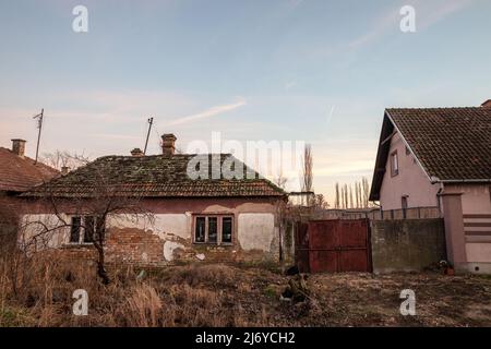 Foto di una fattoria abbandonata in Vojvodina, in Serbia, con la facciata della sua casa principale gravemente danneggiata e decadente. Foto Stock