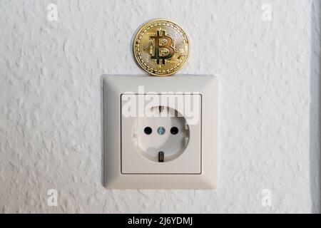 Bitcoin in piedi su una presa di alimentazione. Crypto Currency BTC che viene estratto con un elevato consumo energetico a causa della quantità di processi minerari. Foto Stock