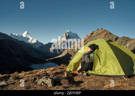 donna asiatica donna camper seduta in tenda godendo la luce del mattino presto con gli occhi chiusi nel parco nazionale yading, contea daocheng, sichuan Foto Stock
