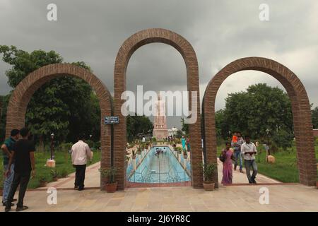 I visitatori alle porte curve che conducono a una statua in pietra arenaria alta 80 piedi del Buddha in piedi a Sarnath, alla periferia di Varanasi, Utar Pradesh, India. Costruita dal 1997 al 2011, la statua fu il risultato di uno sforzo congiunto tra Thailandia e India. Foto Stock