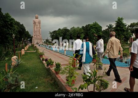 I visitatori camminano verso una statua in pietra arenaria alta 80 piedi del Buddha in piedi a Sarnath, alla periferia di Varanasi, Utar Pradesh, India. Costruita dal 1997 al 2011, la statua fu il risultato di uno sforzo congiunto tra Thailandia e India. Foto Stock