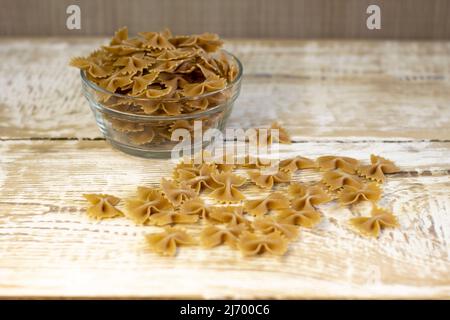 La pasta scura a grana intera si infila su un piatto marrone su uno sfondo chiaro di legno ruvido con fuoco selezionato Foto Stock