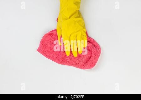 La mano di una casalinga in un guanto di gomma protettivo giallo tiene uno straccio con fibra di microfibra per agente pulente su uno sfondo grigio. Detergente per v Foto Stock