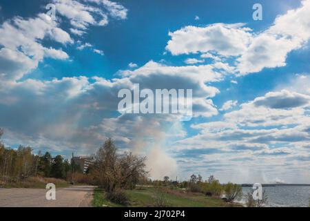 Fumo da incendi boschivi sul lato opposto del lago. Cielo blu con nuvole di cumulo. Foto Stock