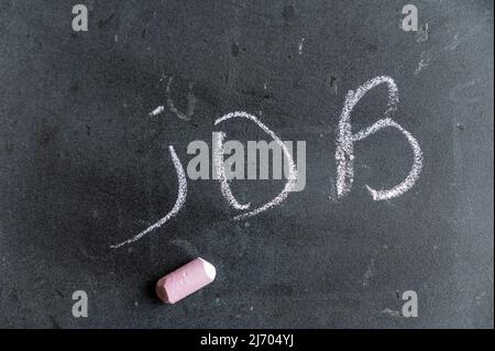 La parola JOB viene scritta su una superficie nera. Testo scritto a mano in gesso rosa su una lavagna sporca. Foto Stock