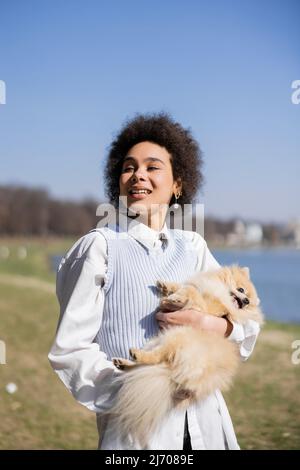 compiacente donna afroamericana che tiene in braccio il cane pomeraniano Foto Stock