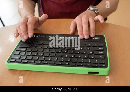 Un uomo cieco utilizza un computer con un display Braille e una tastiera per computer. Dispositivo incluso. Foto Stock