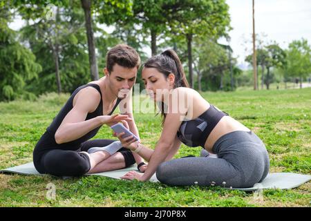 Coppia sportiva seduta su un tappetino che controlla lo smartphone per nuove pose yoga. Foto Stock