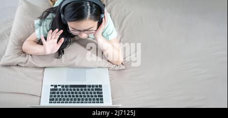 Bella donna asiatica usando zoom meeting e fare video facetime, sociale distanziamento durante il periodo pandemico covid sulla sua camera da letto con un verde pastello Foto Stock