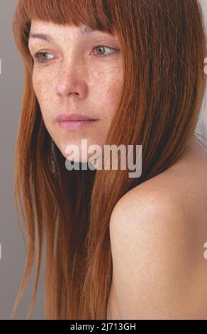 Ritratto di donna caucasica di mezza età con capelli rossastri e greckles guardando da parte su sfondo grigio Foto Stock