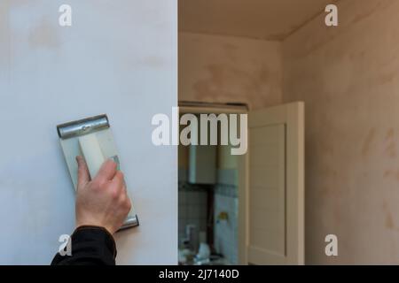 L'appaltatore utilizza una cazzuola per carteggiare il soffitto a secco durante la ristrutturazione della stanza Foto Stock