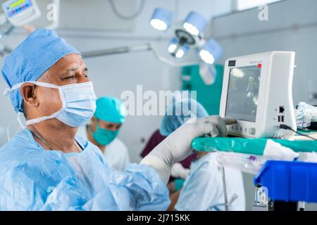 Chirurgo in uniforme che utilizza il monitor per il funzionamento al paziente in sala operatoria - concetto di tecnologia, assistenza sanitaria e trattamento Foto Stock