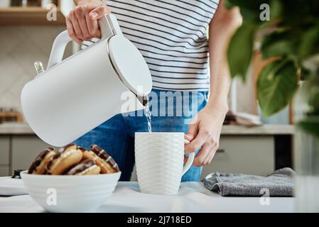 Tempo del tè, Donna versare acqua bollita dal bollitore elettrico in una tazza per preparare il tè, la prima colazione del mattino in cucina Foto Stock