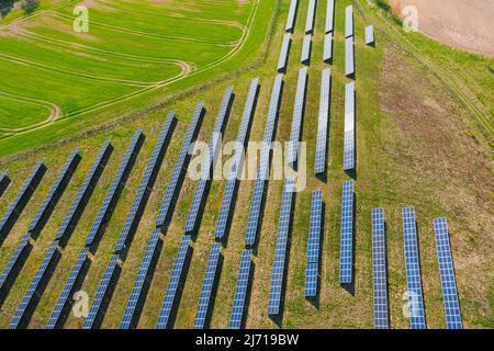 Pannelli solari su una collina sovrastati di verde, illuminati dalla luce del sole. Vista dal drone. Foto Stock