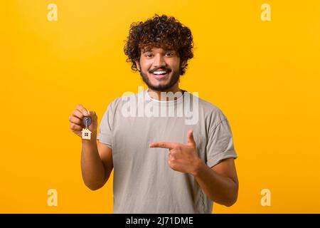 Ragazzo indiano giovane felice mostrando le chiavi e punti dito su di esso in piedi isolato su giallo, uomo ispanico multirazziale felice con le chiavi Foto Stock