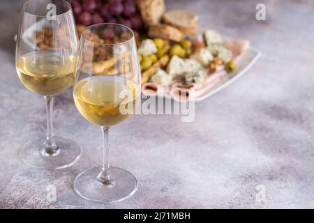 Due bicchieri di vino bianco e la piastra con stuzzichini vari. Formaggio blu, olive, baguette a fette, grissini, prosciutto, uva e i dadi. Vino set snack backg Foto Stock