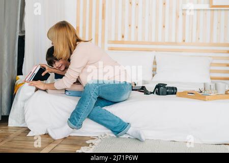 Sorridendo ragazzo scuola caucasico che gioca con mamma sulla tavoletta. Bambino nipote divertirsi con la nonna mentre si gioca a giochi mobili su Foto Stock