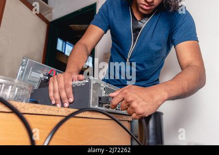 Giovane uomo tecnico di computer brunette afro che ripara il computer a casa, installando i componenti della CPU sulla scrivania. Foto Stock