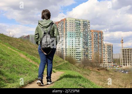 Donna guarda le nuove case in piedi su verde collina, paesaggio urbano in primavera. Settore edile e concetto immobiliare Foto Stock