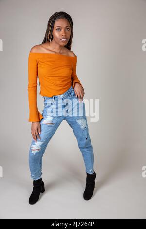 Studio shot di una giovane donna nera con vintage top arancione e i jeans larghi in posa su uno sfondo bianco Foto Stock