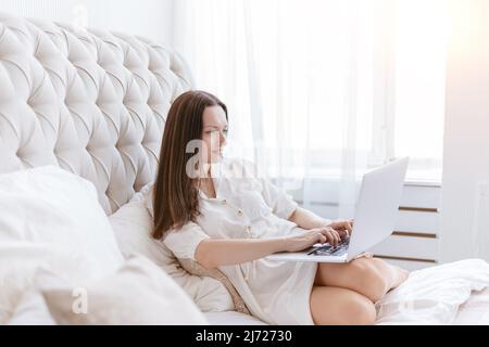 giovane donna con computer portatile seduto sul letto nella sua camera da letto. Foto Stock